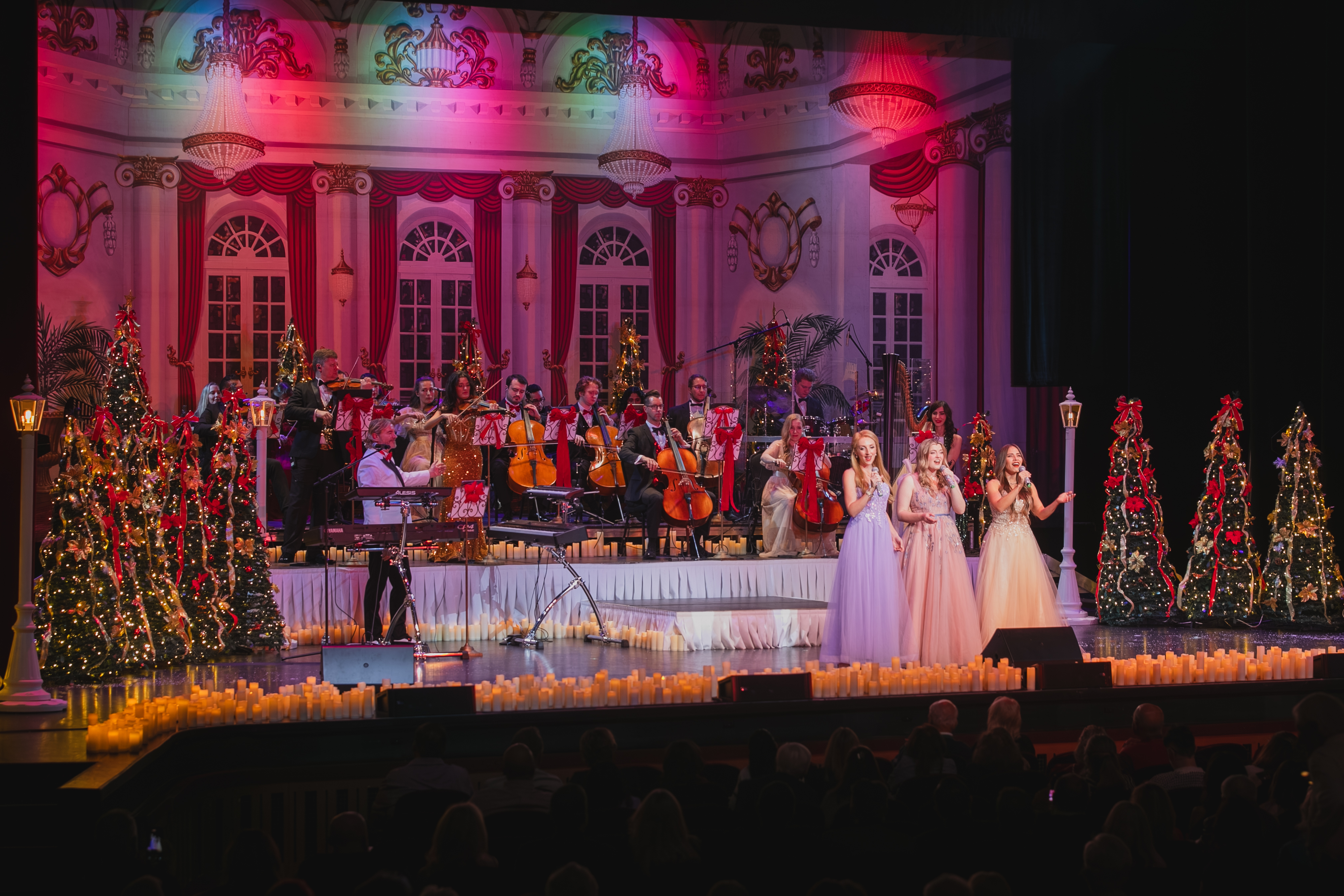 Full stage view of vocalists and orchestra with candlelit holiday set